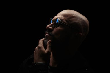 Koyu bir arka plan üzerinde güneş gözlüğü gri sakallı pensive kel adam