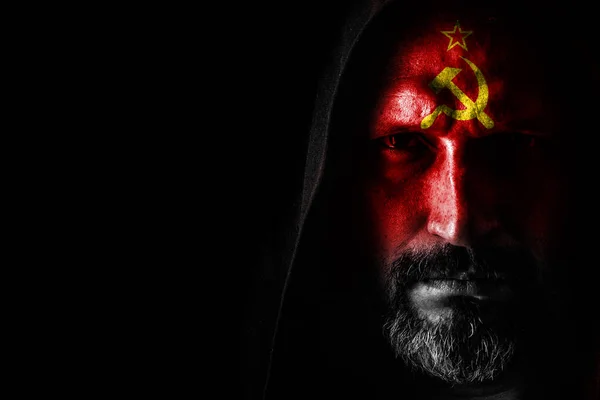 Een brute man met een grijze baard, met de vlag van de USSR op zijn gezicht, in een capuchon met scherpe schaduwen op een zwarte achtergrond. Ruimte kopiëren — Stockfoto