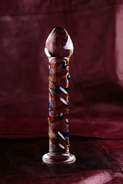 Glass dildo on a red leather background 