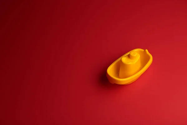 Pequeno navio de brinquedo de plástico amarelo no fundo vermelho com espaço de cópia . — Fotografia de Stock