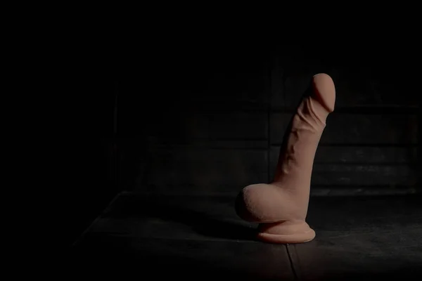 Very realistic dildo with balls on dirty dark background with hard light and shadow