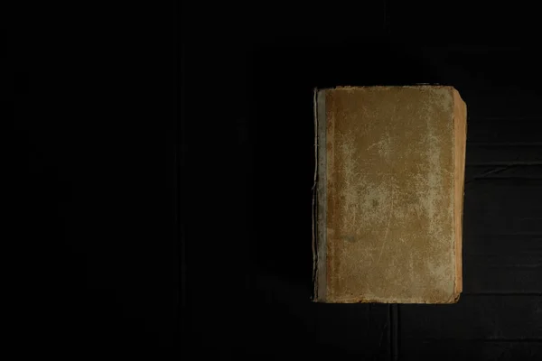 Vintage book with very old shabby cover on dirty black background with hard light and shadow. — Stock Photo, Image