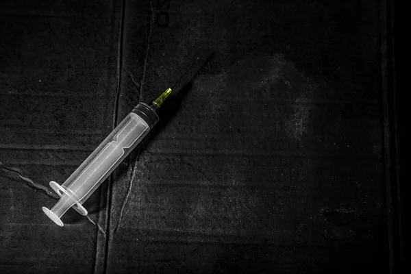 Pusta jednorazowa strzykawka na brudnym czarnym tle z dramatycznym światłem i cieniem — Zdjęcie stockowe