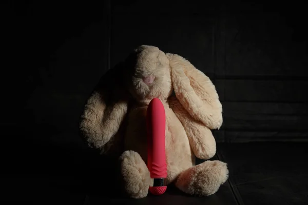 Coniglietto giocattolo morbido con dildo rosa su uno sfondo scuro sporco con luce dura e ombre. Sesso maniaco o pazzo coniglio concepimento . — Foto Stock