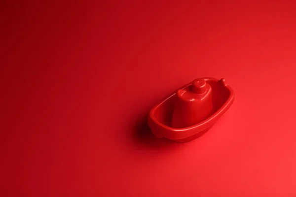 Kleines rotes Plastikspielzeugschiff auf rotem Hintergrund mit Kopierraum. — Stockfoto