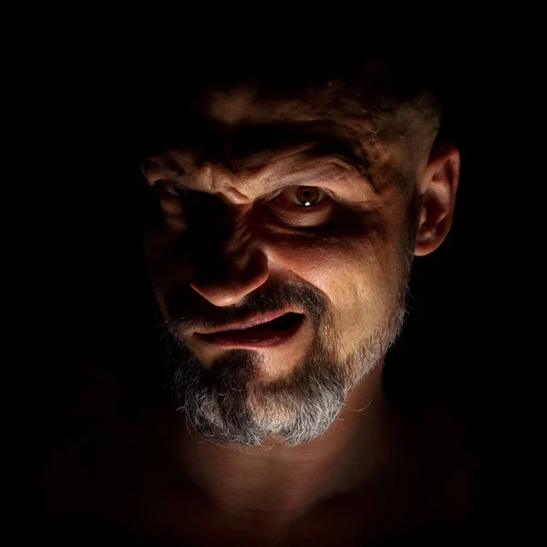 Комедийный, сказочный злодей или негативный персонаж. Лицо с бородой человека гримаса на темном фоне с острыми тенями . — стоковое фото