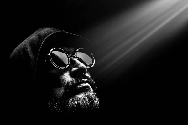 Güneş gözlüklü, sakallı, kaputunda vahşi adam, ışık ışınlarına bakıyor. Umut. — Stok fotoğraf