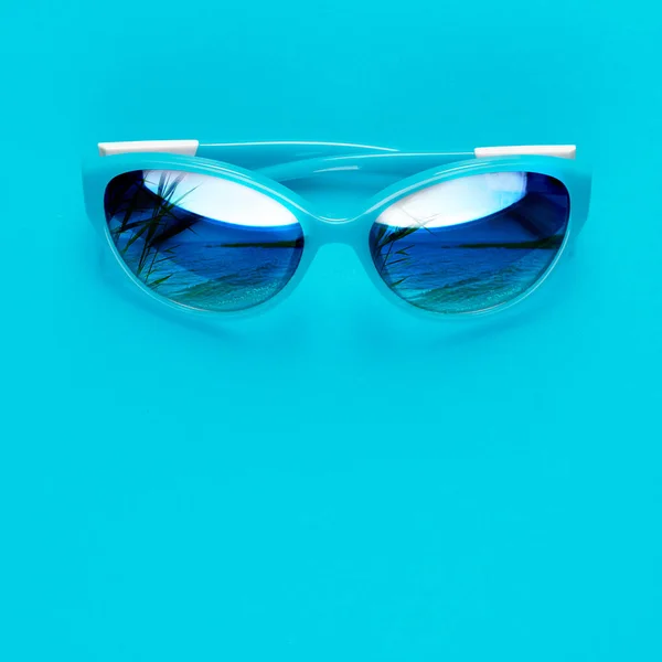 Elegantes gafas azules, que reflejan el mar sobre un fondo azul. El verano se acerca concepto . —  Fotos de Stock