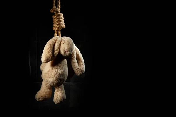 Кроличья игрушка, повешенная на толстой плетеной веревке на темном фоне. Концепция самоубийства . — стоковое фото