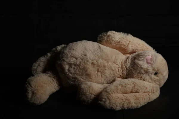 Мягкая игрушка кролика на грязном темном фоне в луче жесткого света с тенью. Потерянное детство — стоковое фото