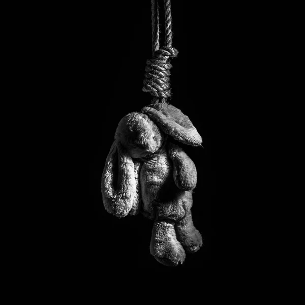 Kaninchenspielzeug, aufgehängt an einem dicken geflochtenen Seil auf dunklem Hintergrund. Selbstmordgedanken. — Stockfoto