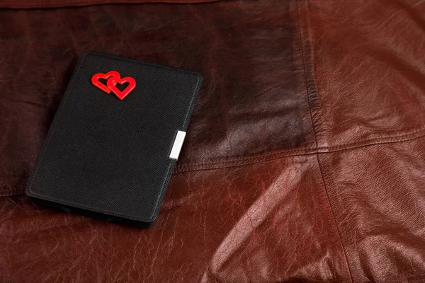 Electronic book in case with two hearts on leather background. Romantic book concept.