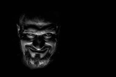 Keskin gölgeler ile karanlık bir arka plan karşı sakallı bir adam grimace ile yüz. Komedi, kopya alanı ile muhteşem kötü adam veya negatif karakter anlayışı.