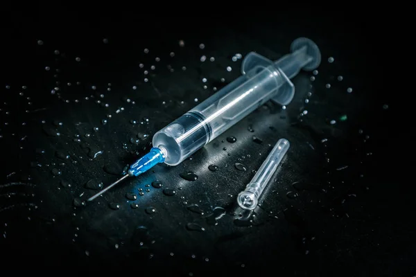Uma seringa com um líquido transparente repousa sobre um fundo escuro sujo coberto com gotas . Fotografias De Stock Royalty-Free