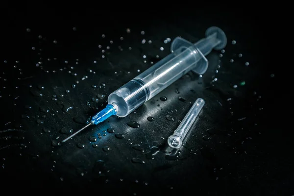 A syringe with a clear liquid lies on a dirty dark background covered with drops. Royalty Free Stock Photos