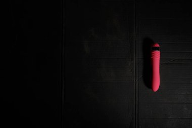 Simple pink dildo on dirty black background with hard light and shadows with copyspace.