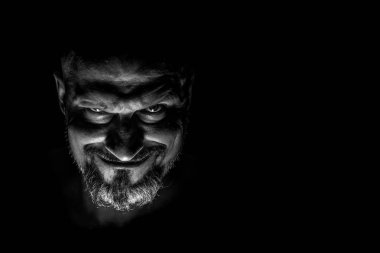  Keskin gölgeler ile karanlık bir arka plan karşı sakallı bir adam grimace ile yüz. Komedi, kopya alanı ile muhteşem kötü adam veya negatif karakter anlayışı.