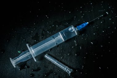 Açık sıvı olan bir şırınga, damlalar ile kaplı kirli karanlık bir arka planda yatıyor.