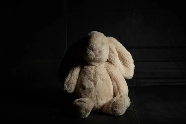 Soft Toy Bunny op een vuile donkere achtergrond in de balk van hard licht met schaduw. Verloren jeugd concept — Stockfoto