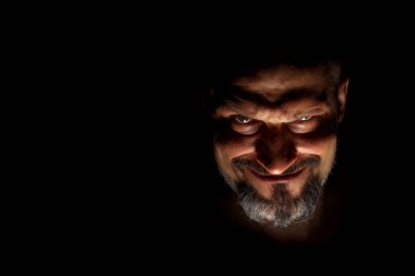  Keskin gölgeler ile karanlık bir arka plan karşı sakallı bir adam grimace ile yüz. Komedi, kopya alanı ile muhteşem kötü adam veya negatif karakter anlayışı.