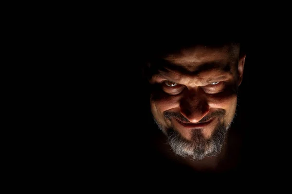  Keskin gölgeler ile karanlık bir arka plan karşı sakallı bir adam grimace ile yüz. Komedi, kopya alanı ile muhteşem kötü adam veya negatif karakter anlayışı.