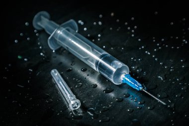 Açık sıvı olan bir şırınga, damlalar ile kaplı kirli karanlık bir arka planda yatıyor.