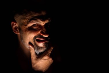  Keskin gölgeler ile karanlık bir arka plan karşı sakallı bir adam grimace ile yüz. Komedi, kopya alanı ile muhteşem kötü adam veya negatif karakter anlayışı.