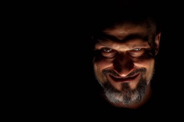  Face with a bearded man grimace against a dark background with sharp shadows. Comedic, fabulous villain or negative character conception with copy space. clipart