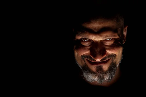  Keskin gölgeler ile karanlık bir arka plan karşı sakallı bir adam grimace ile yüz. Komedi, kopya alanı ile muhteşem kötü adam veya negatif karakter anlayışı.