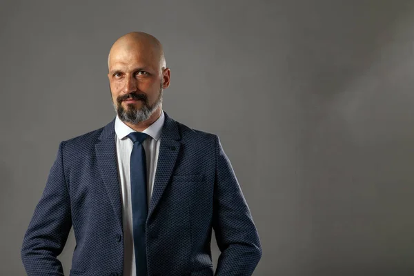 Cute young bald bearded businessman in a classic suit on a gray background with copy space