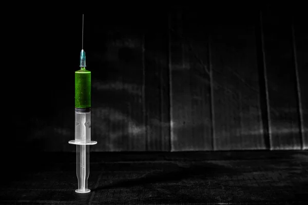 在肮脏的黑暗背景上用绿色液体的注射器, 有锐利的光线和阴影。毒品是毒药的概念. — 图库照片