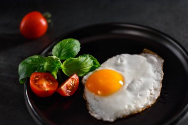 Domatesli yumurta ve siyah tabakta fesleğen.