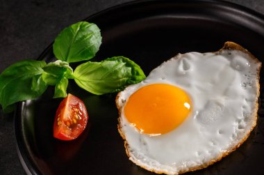 Domatesli yumurta ve siyah tabakta fesleğen.