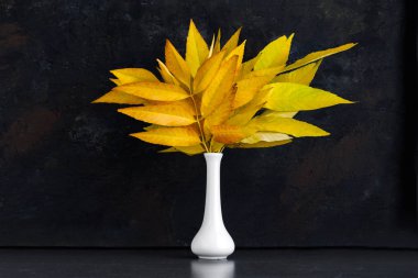 Beyaz vazoda sarı sonbahar yaprakları