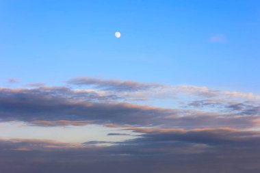 Beyaz bir ay ve leylak-turuncu bulutlarla akşam gökyüzü