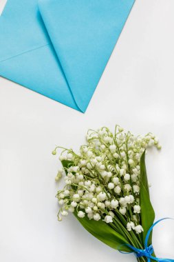 Vadi zambakları ve beyaz bir masanın üzerinde mavi bir zarf.