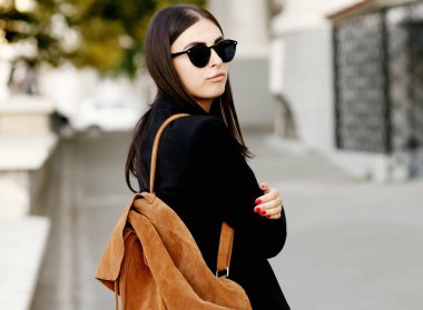 Güzel genç öğrenci hippi kız sağlıklı düz saçlı bir siyah ceket ve güneş gözlüğü takıyor. Sokak stili