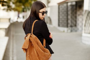 Güzel genç öğrenci hippi kız sağlıklı düz saçlı bir siyah ceket ve güneş gözlüğü takıyor. Sokak stili