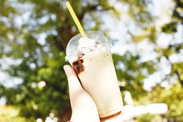 昼間に公園のテーブルでコーヒー カフェラテ クリームとチョコレートの大きな部分を保持している人の手のクローズ アップ — ストック写真