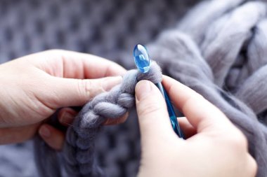 Mavi iğne ile örgü gri örgü modeli üzerinde eller closeup 