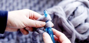 Mavi iğne ile örgü gri örgü modeli üzerinde eller closeup 