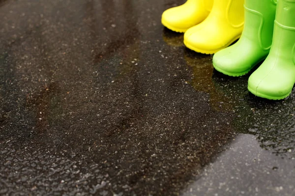 Closeup of childish gum boots placed on wet asphalt at daytime