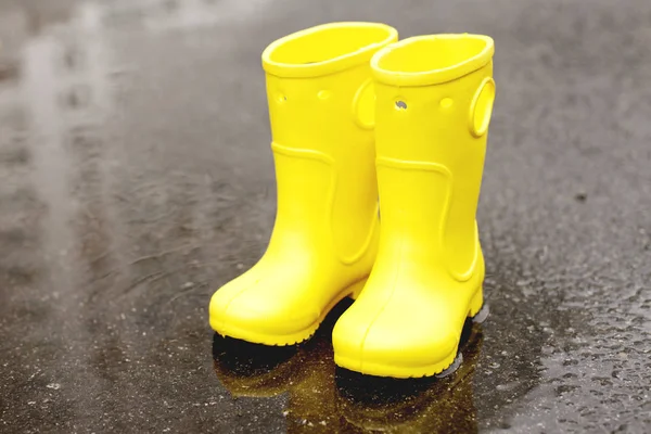 Closeup of childish gum boots placed on wet asphalt at daytime