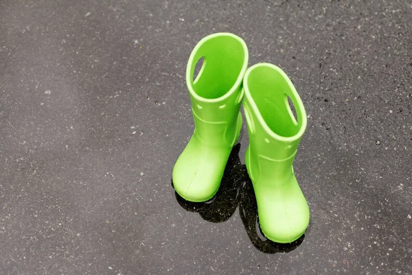 Closeup of childish gum boots placed on wet asphalt at daytime