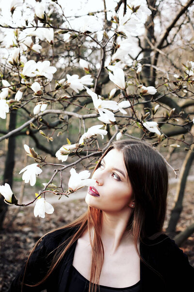 Beauty young woman enjoying nature in spring magnolia flowers. Beautiful brunette girl in Garden with blooming magnolia trees.