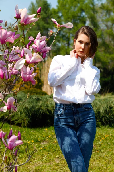 Młody piękny model kobieta stwarzających w ogrodzie kwitnące Magnolie. — Zdjęcie stockowe