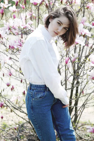若い美しいモデル女性が咲くマグノリアの庭でポーズ. — ストック写真