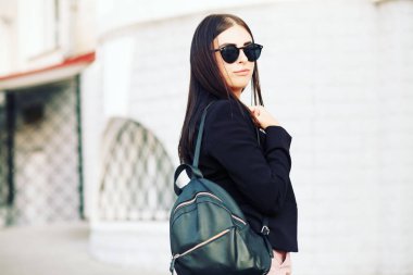 Güzel genç öğrenci hippi kız sağlıklı düz saçlı bir siyah ceket ve sırt çantası takmış. Sokak stili.