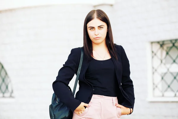 Beautiful young student hipster girl with healthy straight hair wearing a black jacket and backpack. Street style.