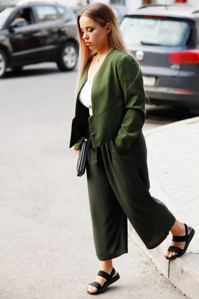 Young blonde woman in green outfit walking by street